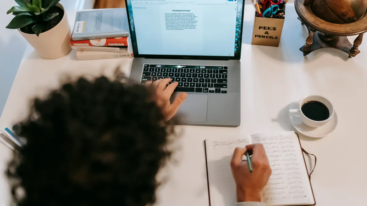 person drafting content beside a laptop and notebook